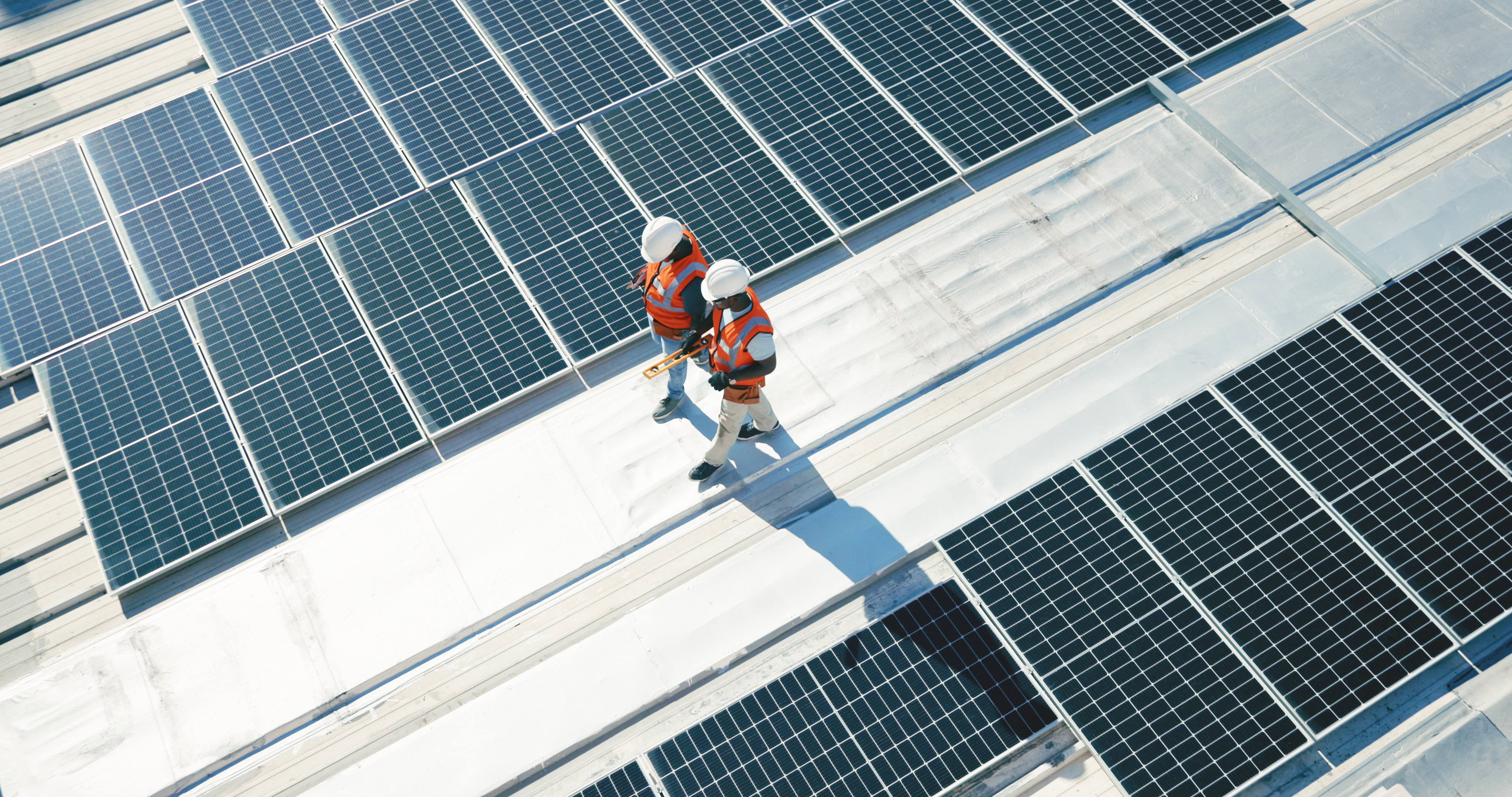 Symbolbild: zwei Wartungstechniker, die eine Solaranlage am Dach begehen